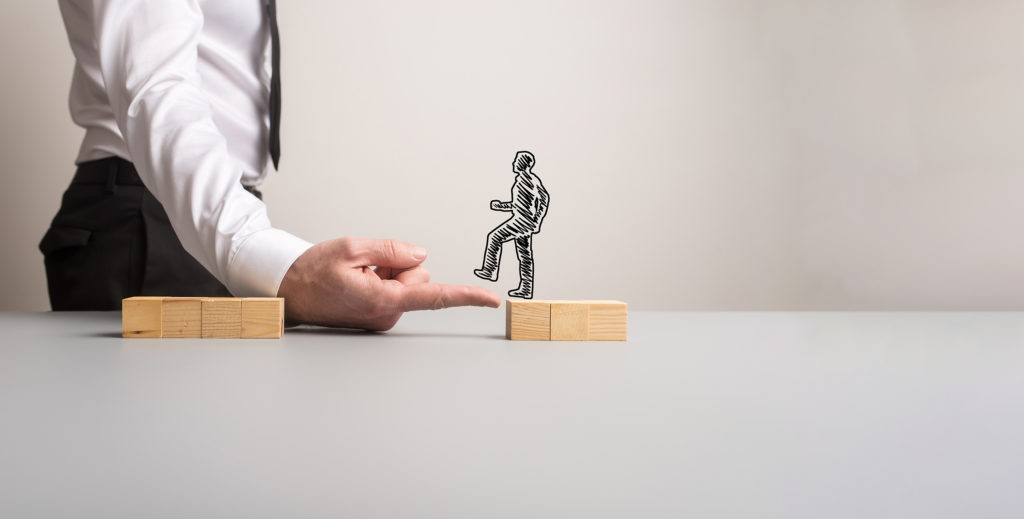 Businessman making a bridge of his finger for a silhouetted businessman to walk across one pile of wooden blocks to the other in a conceptual image. With copy space.